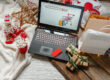 Holiday-themed scene with a laptop, gift boxes, and festive decorations.