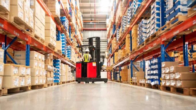 warehouse with products stacked on shelves and a worker on a forklift